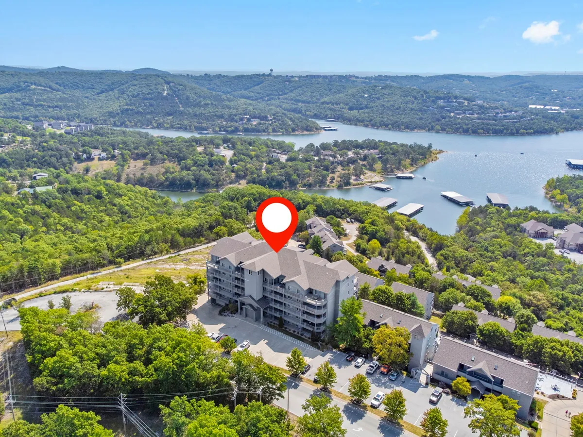 This image captures a tranquil scene featuring a shimmering lake with mountains in the background, the condo building in the foreground, and a road leading towards the water. The view is open, evoking a sense of peaceful escape and the promise of outdoor adventures.