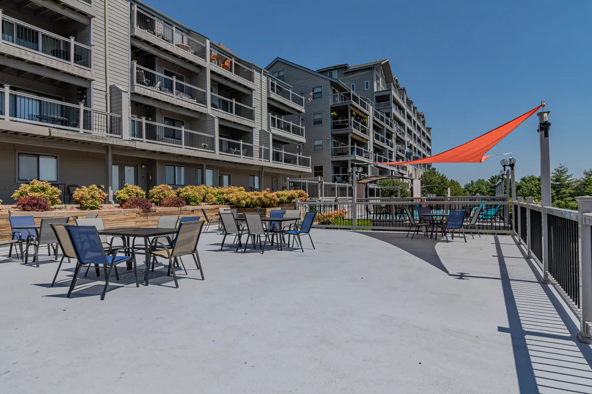 This exterior shot features a friendly outdoor seating area adorned with colorful flowers and an orange shade sail. Balconies on the building above suggest private outdoor spaces, while the scene captures a relaxed and social atmosphere for outdoor dining or evening gatherings.