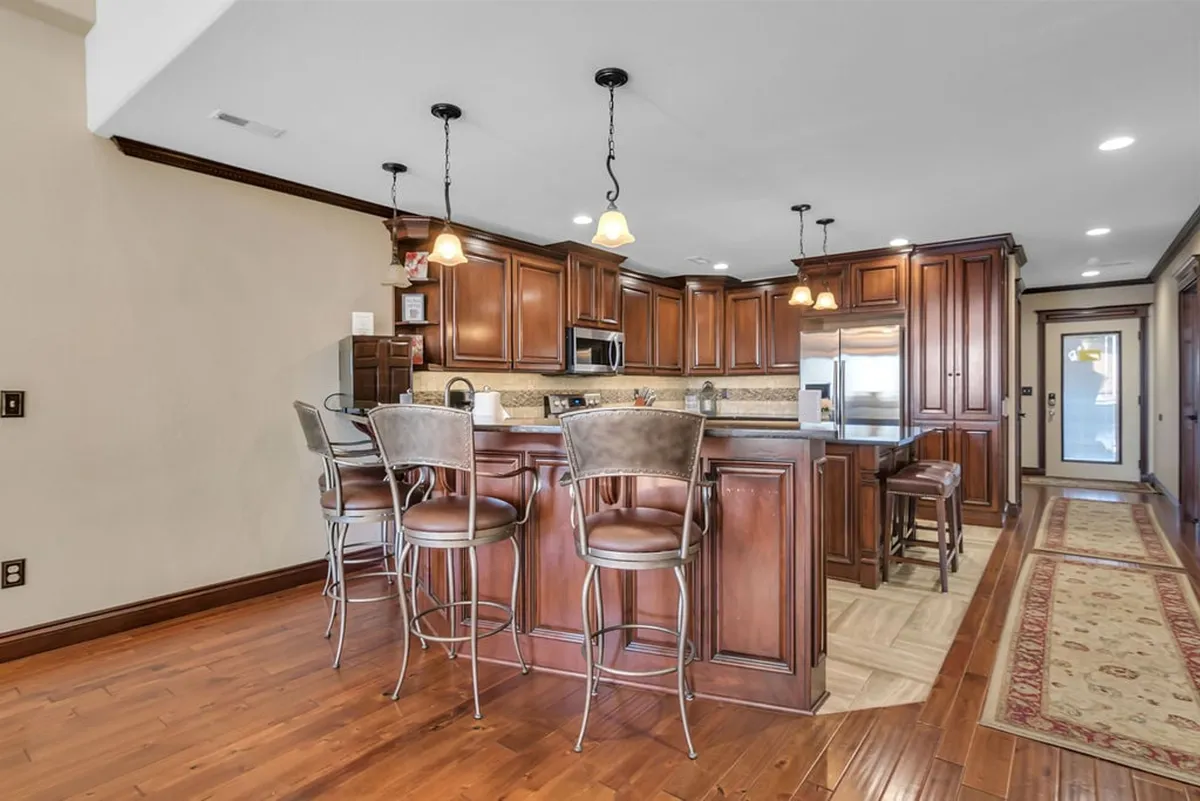A welcoming kitchen scene featuring wooden cabinetry, a central island with seating, and visible kitchen appliances. The arrangement suggests an inviting space for family gatherings, dinner parties, or casual entertaining, with a warm, homey feel.