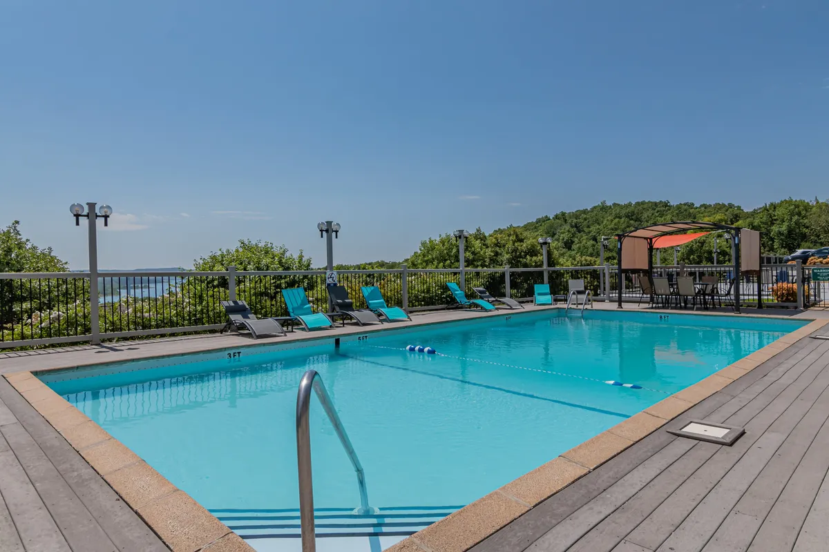 This image presents a sparkling outdoor swimming pool surrounded by lounge chairs, a canopy area for shade, and lush greenery. The inviting setting is perfect for sunbathing, swimming, and socializing, evoking a laid-back resort atmosphere.