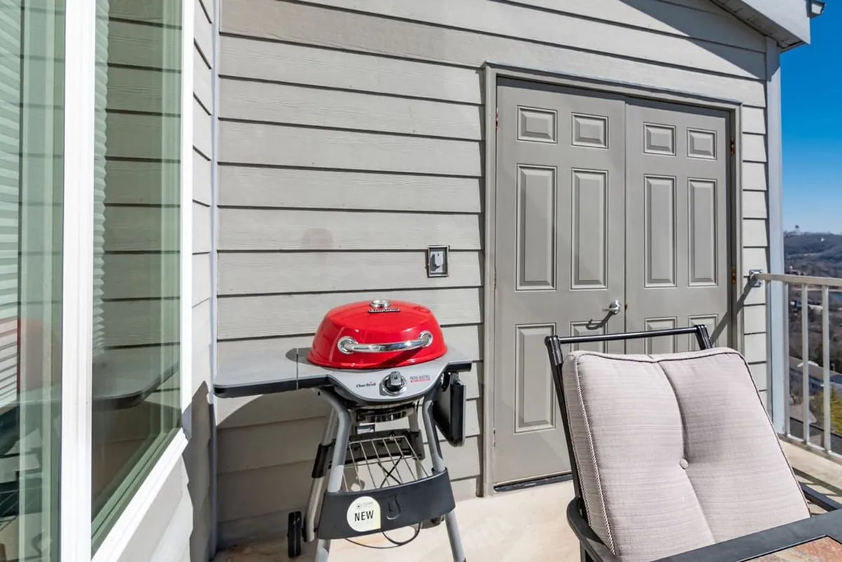 An inviting deck setup features a red grill, a comfortable chair, and double doors leading inside. The arrangement hints at sunset gatherings, casual barbecues, and an easy flow between indoor and outdoor living.