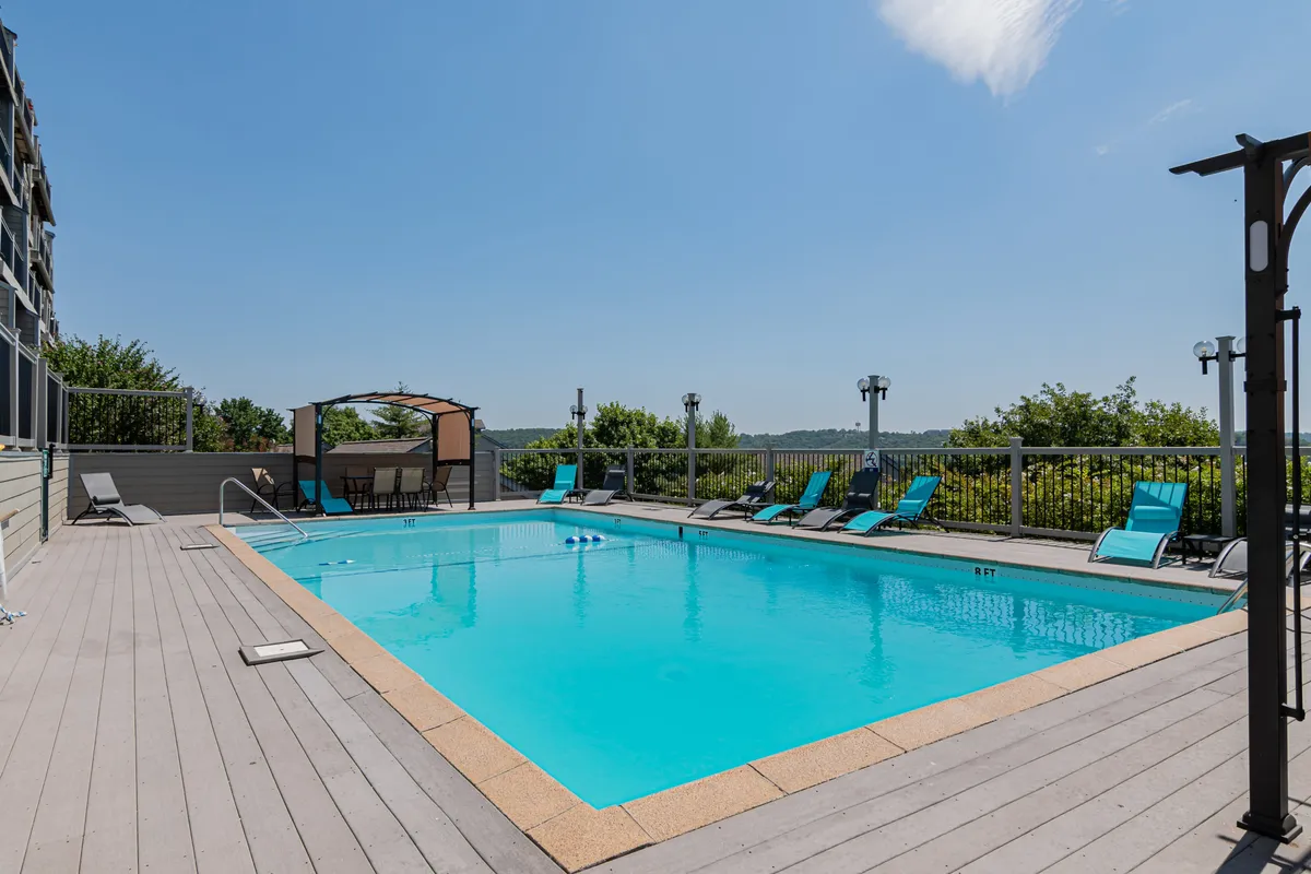 The exterior scene showcases a vibrant swimming pool surrounded by lounge chairs, a cabana, and lush greenery. The area is inviting and designed for relaxation or socializing on sunny days.