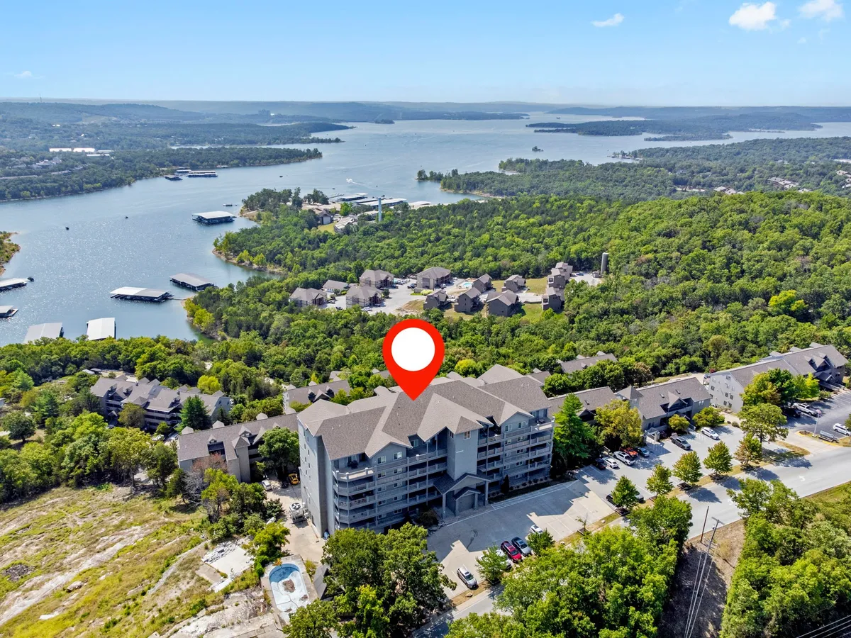 A scenic exterior view of Table Rock Lake, with the lake stretching across the foreground and buildings nestled among vibrant greenery. The tranquil waters and open sky capture the allure of lake access and outdoor adventure.