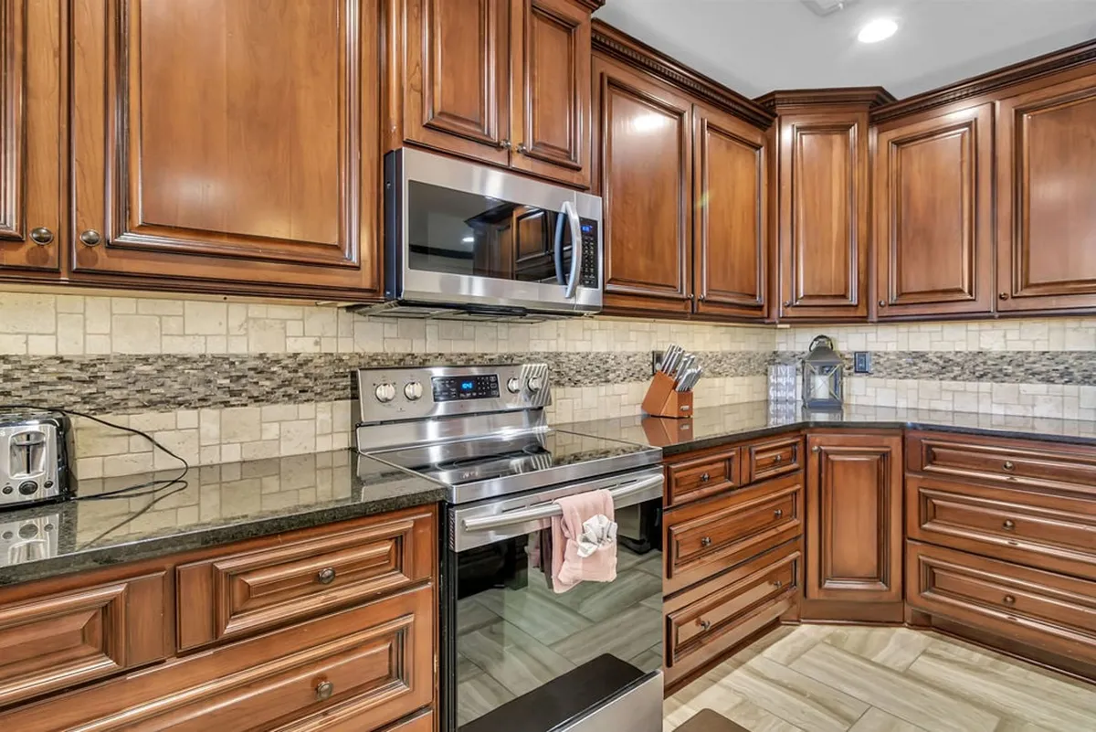 The kitchen’s wooden cabinetry is complemented by modern stainless steel appliances and a granite countertop, with a cheerful backsplash tying the look together. Multiple prep spaces and open sightlines suggest ease of entertaining and connection to adjacent living areas.