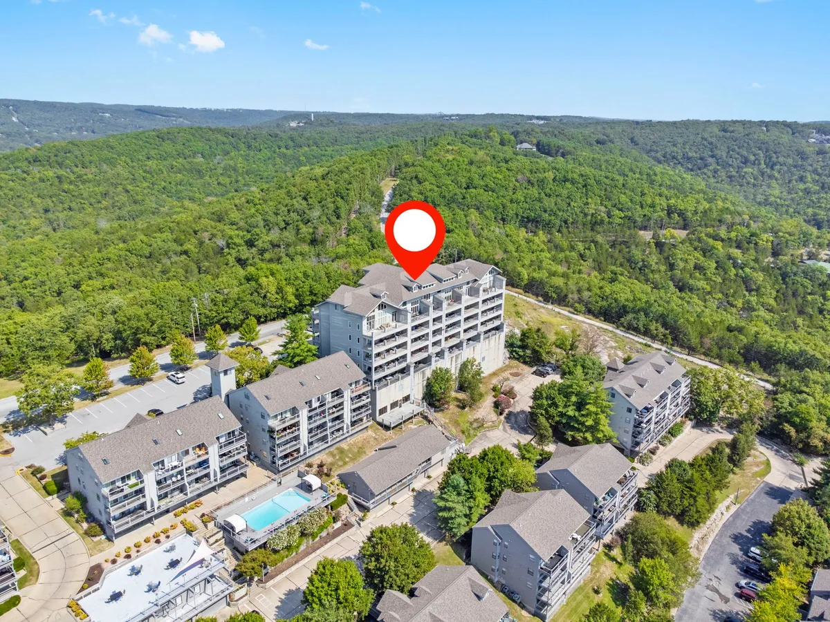 An exterior shot of a multi-story resort building with balconies, a sparkling swimming pool, a generous parking area, and surrounding greenery. The scene conveys a welcoming and tranquil atmosphere, highlighting both leisure and convenience.